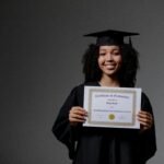 Smiling graduate proudly holding a certificate in cap and gown.
